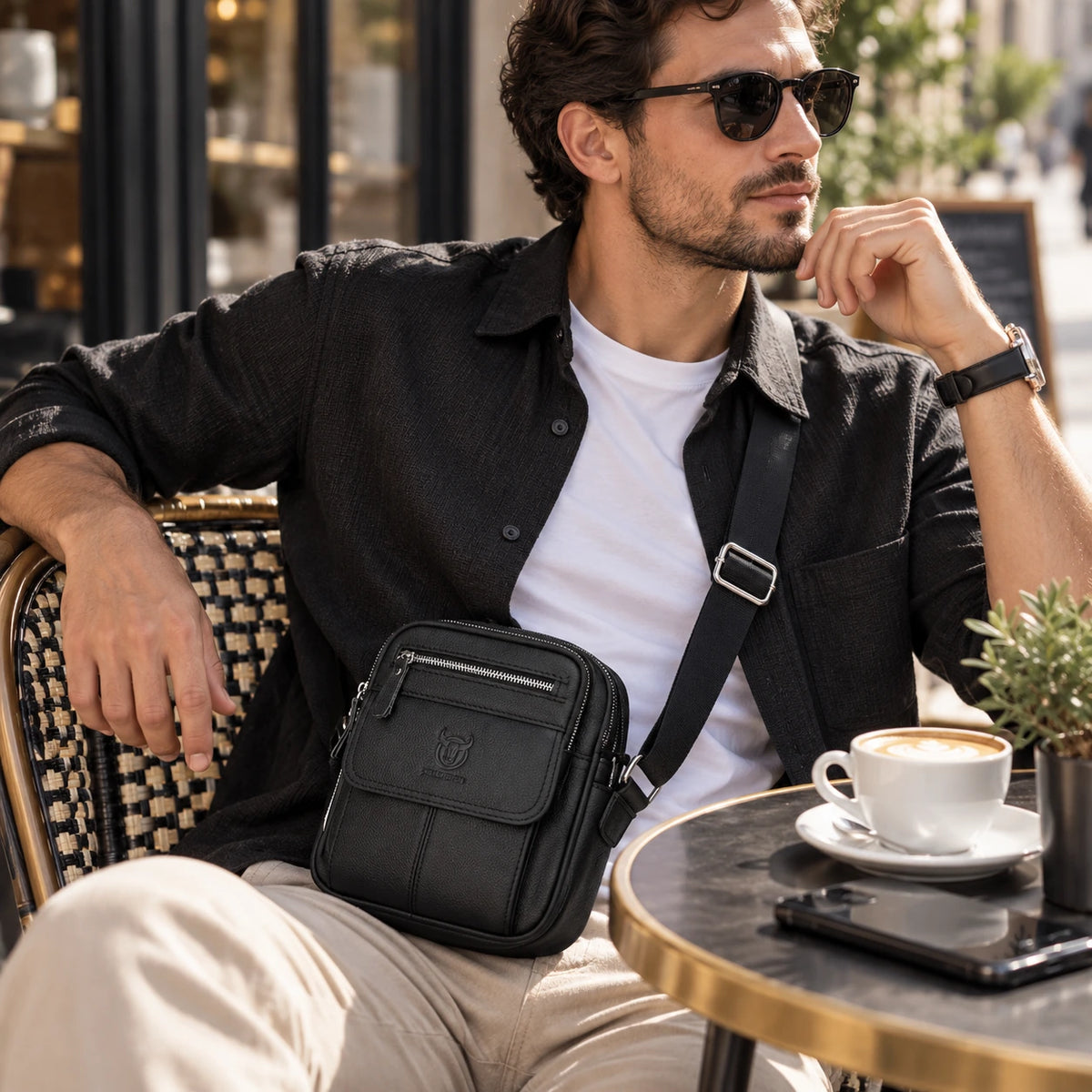 Homme portant une petite sacoche bandoulière noire à une terrasse de café